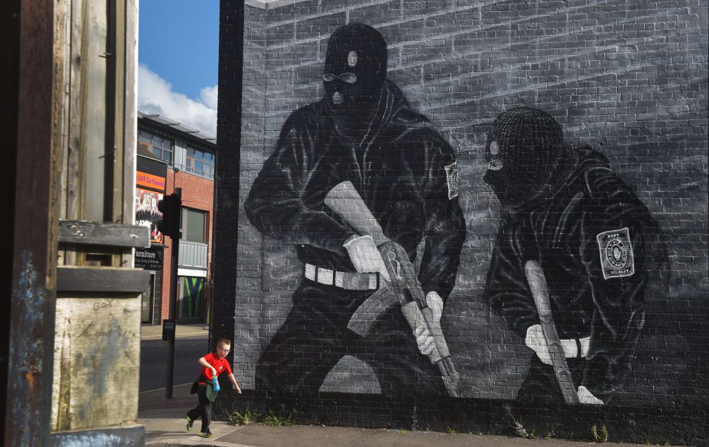 BELFAST, NORTHERN IRELAND - OCTOBER 13: A young boy runs past a loyalist paramilitary mural on the day that the new Loyalist Community Council was launched at the Park Avenue Hotel on October 13, 2015 in Belfast, Northern Ireland. The council has the backing of the three main loyalist paramilitary groups, the UVF, the UDA and the Red Hand Commandos. A joint statement from the three loyalist groups said that they are "re-committing to the principals of the Belfast Agreement" and that they "eschew all violence and criminality". The launch of the new loyalist community council comes against the backdrop of an ongoing crisis at Stormont following following allegations that the IRA were involved in the murder of their former member Kevin McGuigan. (Photo by Charles McQuillan/Getty Images)