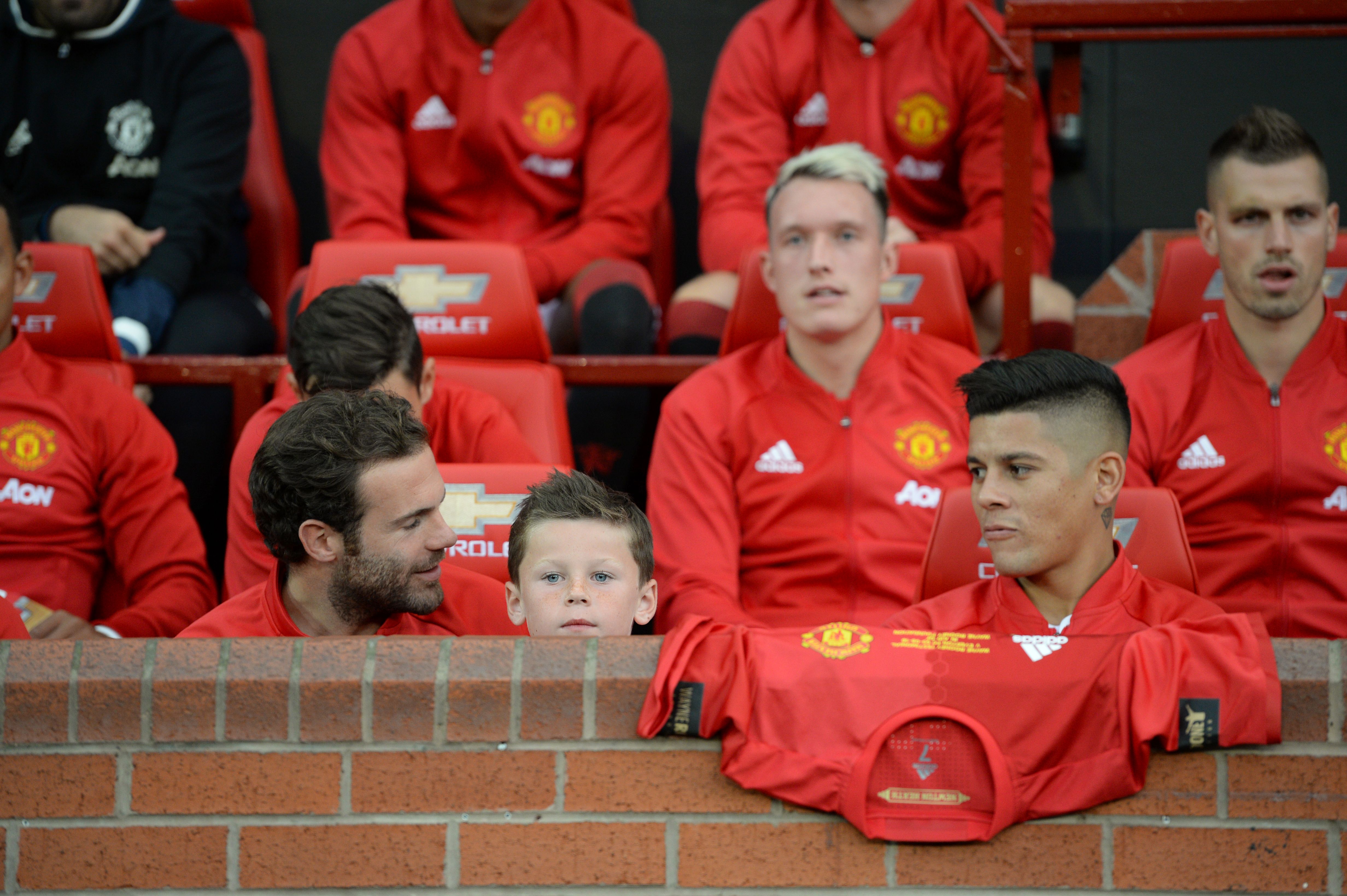 Kai Rooney (C), son of Manchester United's English striker Wayne Rooney, sits on the substitutes bench with Manchester United's Spanish midfielder Juan Mata (L) and Manchester United's Argentinian defender Marcos Rojo (R) before kick off of the friendly Wayne Rooney testimonial football match between Manchester United and Everton at Old Trafford in Manchester, northwest England, on August 3, 2016. / AFP / OLI SCARFF (Photo credit should read OLI SCARFF/AFP/Getty Images)