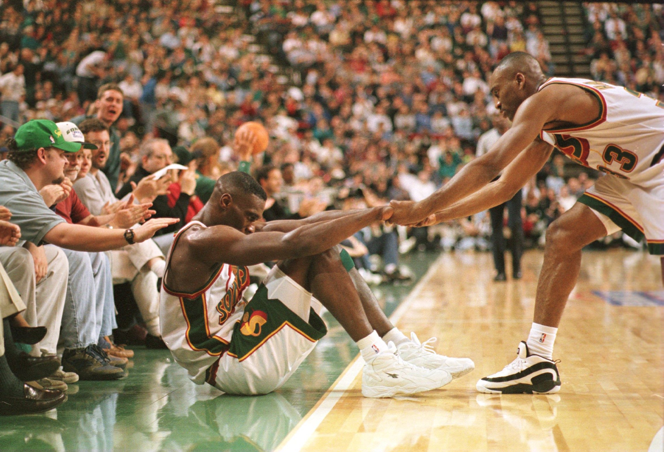 18 May 1996: Hersey Hawkins #33 of the Seattle Supersonics helps teammate Shawn Kemp #40 to his feet as fans cheer them on during the Sonic''s 102-72 game one victory over the Utah Jazz in the NBA Western Conference Finals at Key Arena in Seattle, Washing